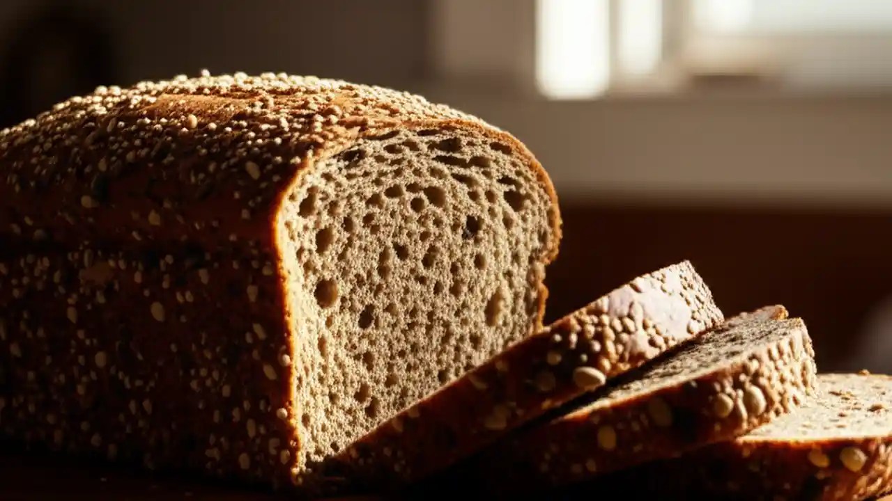 A freshly sliced loaf of Dave's Killer Bread, highlighting its texture and seeds, sits on a rustic wooden cutting board.