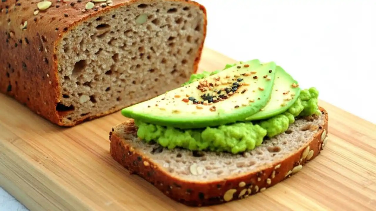 A top-down view of a slice of whole-grain bread on a wooden board, topped with sliced avocado, representing a healthy meal for a person with diabetes.