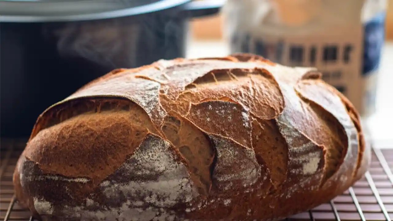 A perfectly baked golden-brown loaf of artisan bread resting on a cooling rack, with steam gently rising from its crust.
