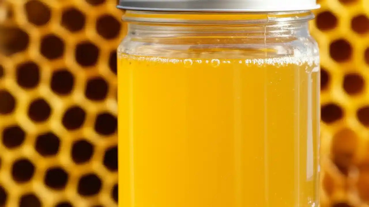 A close-up of clear, golden sugar water in a glass jar, with a honeybee drinking, illustrating perfect bee feed for colony health.