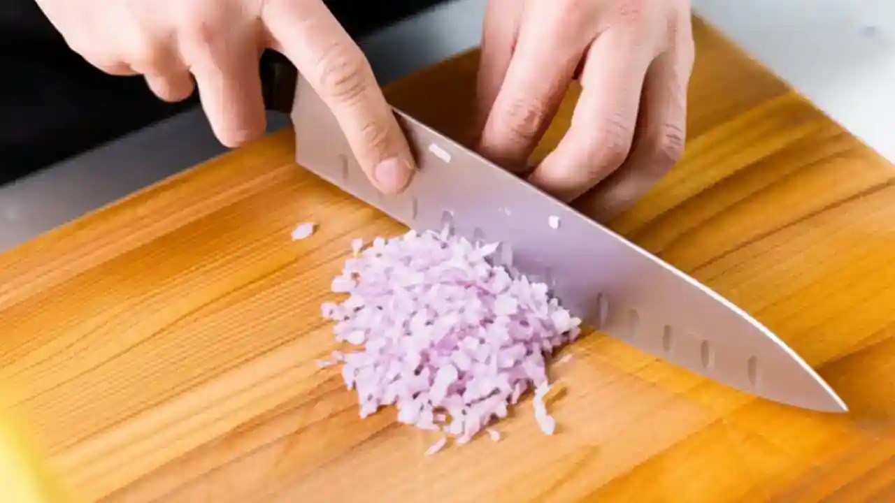 Skilled hands mincing shallots perfectly on a wooden cutting board with a sharp chef's knife.