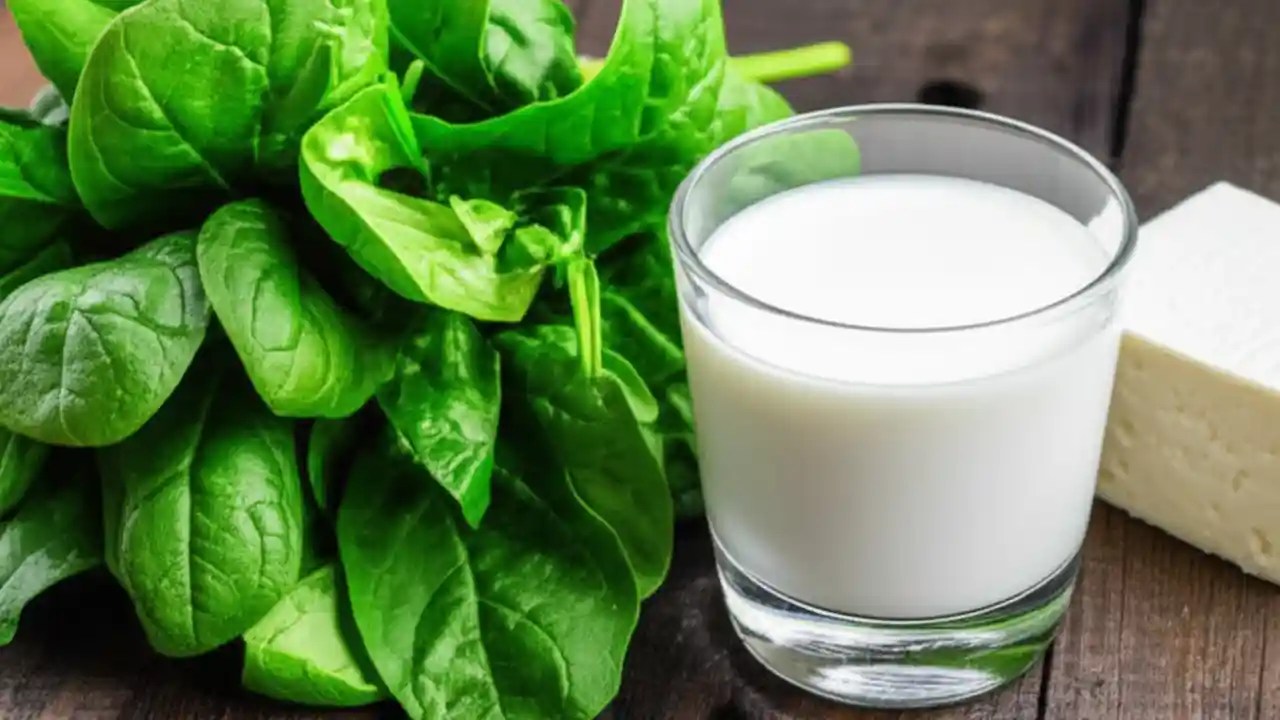 A fresh bunch of spinach next to a glass of milk and cheese, illustrating a comparison of dietary calcium sources and bioavailability.