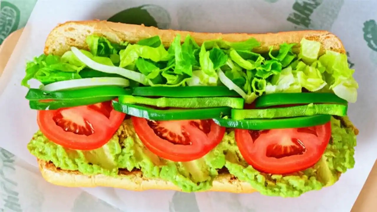 An overhead view of an open Subway sandwich showcasing the variety of fresh vegetable options available, including lettuce, tomatoes, and avocado.