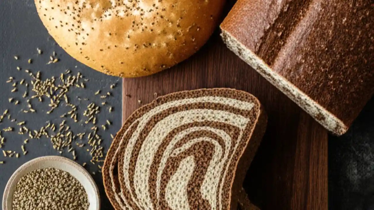 An overhead view of various types of rye bread, including light rye, dark pumpernickel, and marbled rye, arranged on a wooden board.