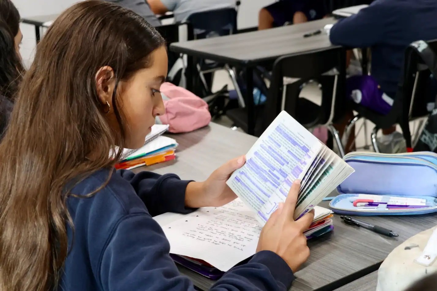 Bright female student engaged in classical learning at Florida Institute of Classical Learning, studying texts with highlighted passages, in a modern classroom setting emphasizing education and classical studies.