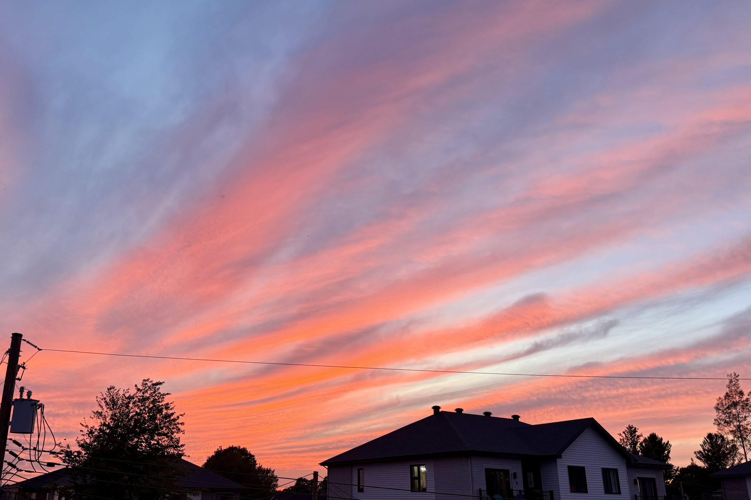 Pink and orange sunset clouds above houses and power lines.