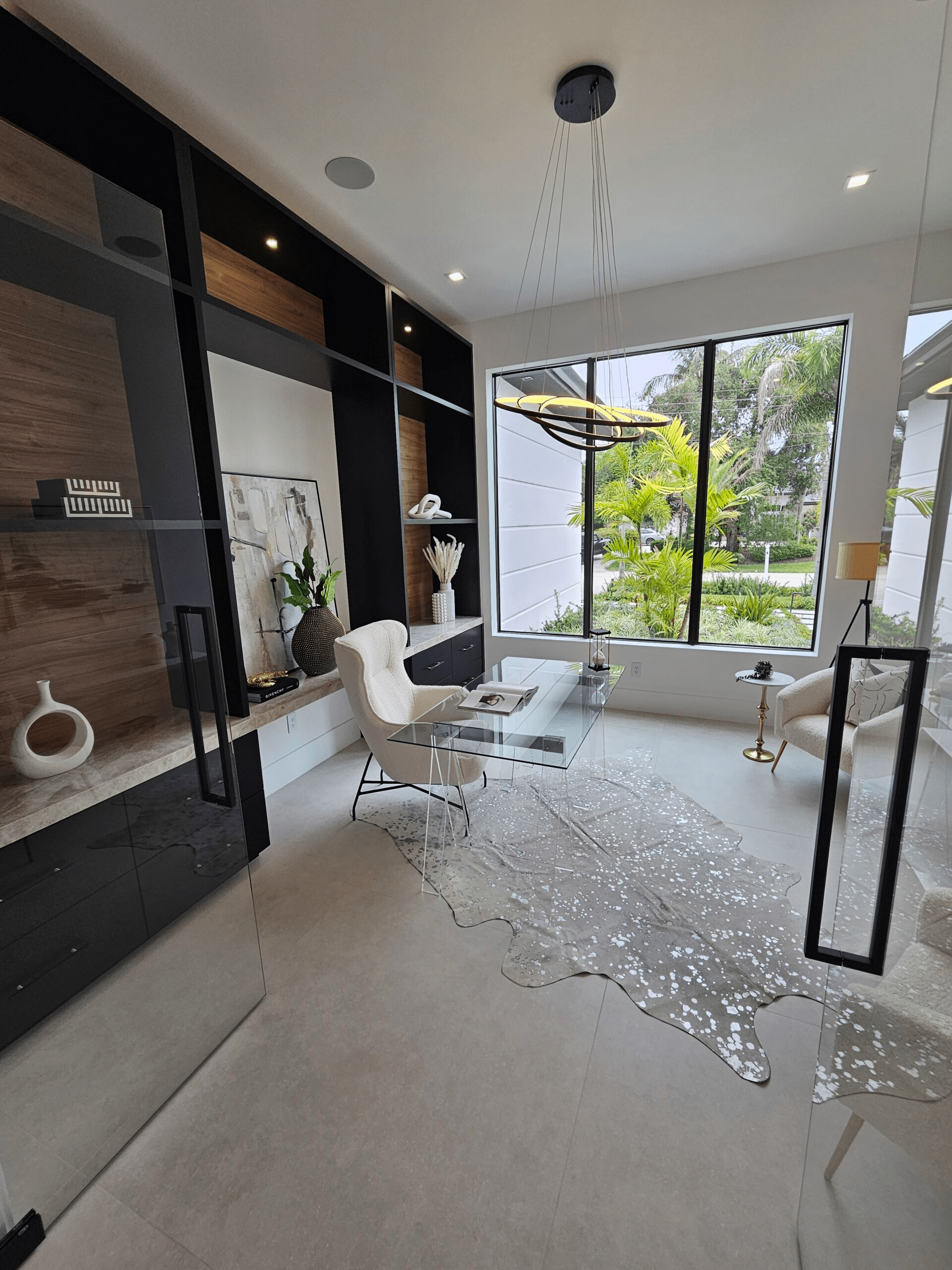 A residential office space with a dark wood accent wall and large window. A glass desk and modern furniture adorn the space.