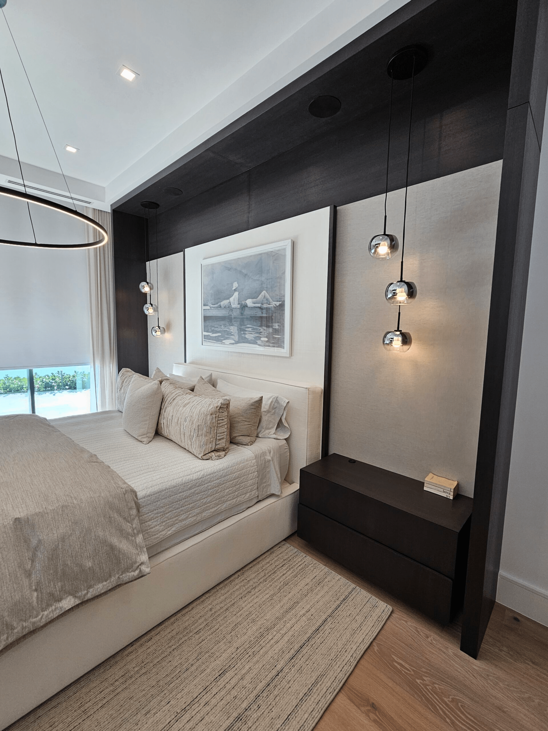 A clean white bedroom with a dark wood accent wall, modern pendent lights, and a large chandelier over the bed.
