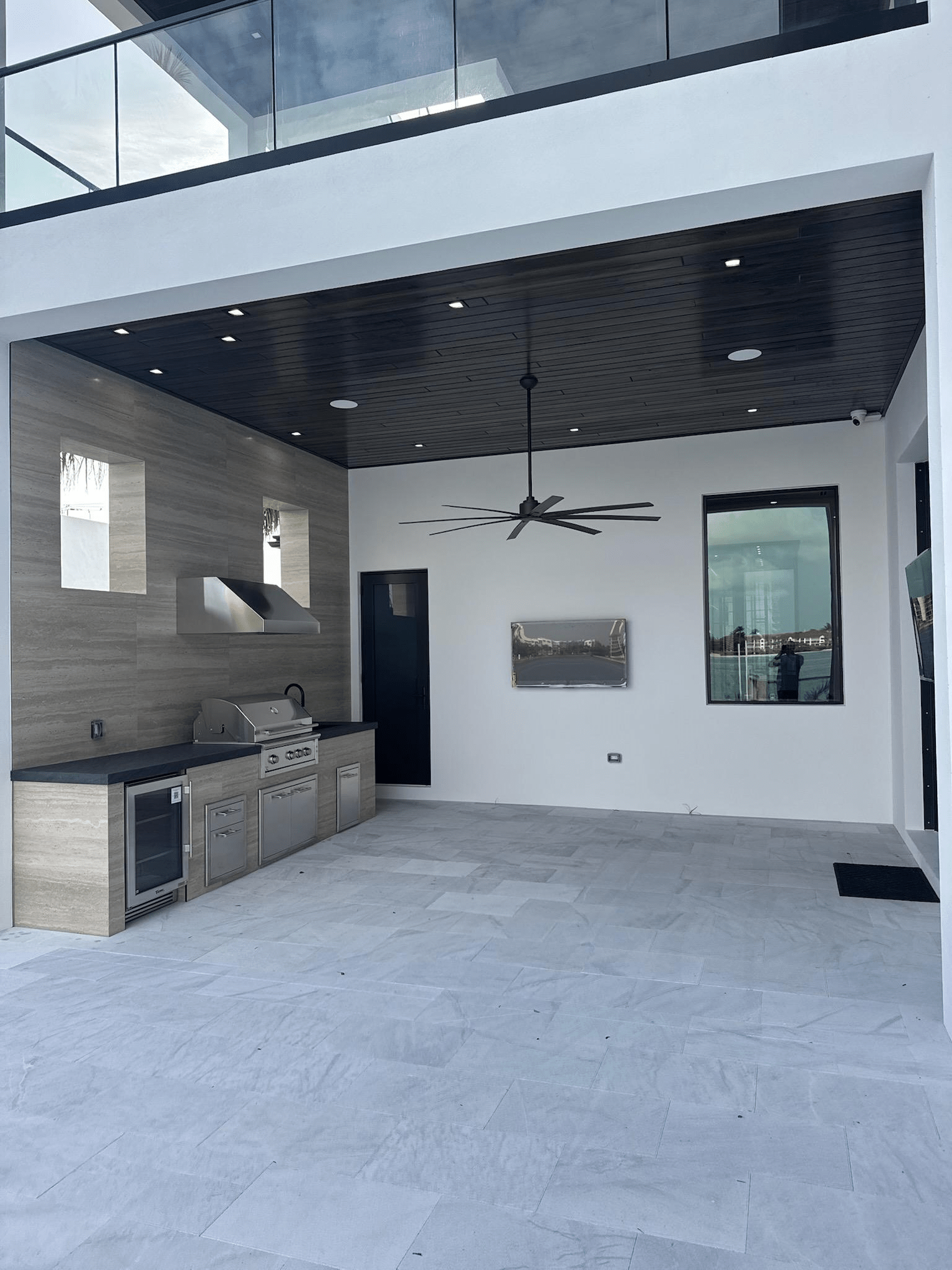 An exterior residential living space with a full cooking and prep counter, recessed lighting, and a dark wood accent ceiling.
