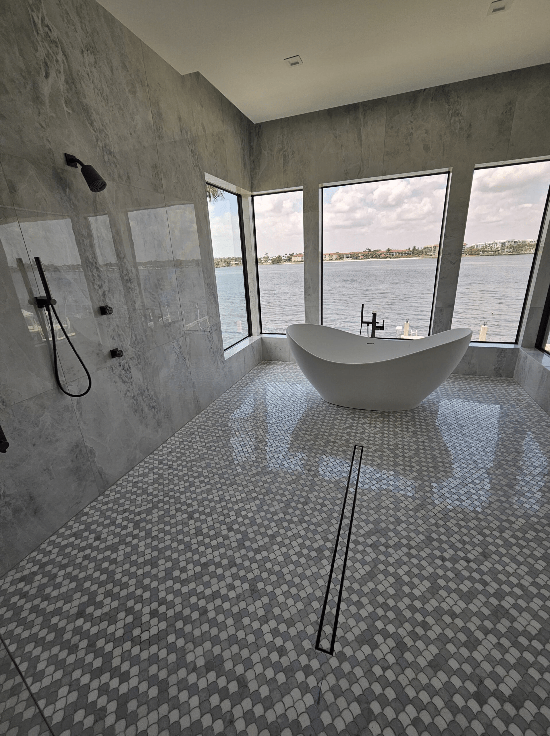 A stunning bathroom with a free standing white tub shown against large windows looking over the water.