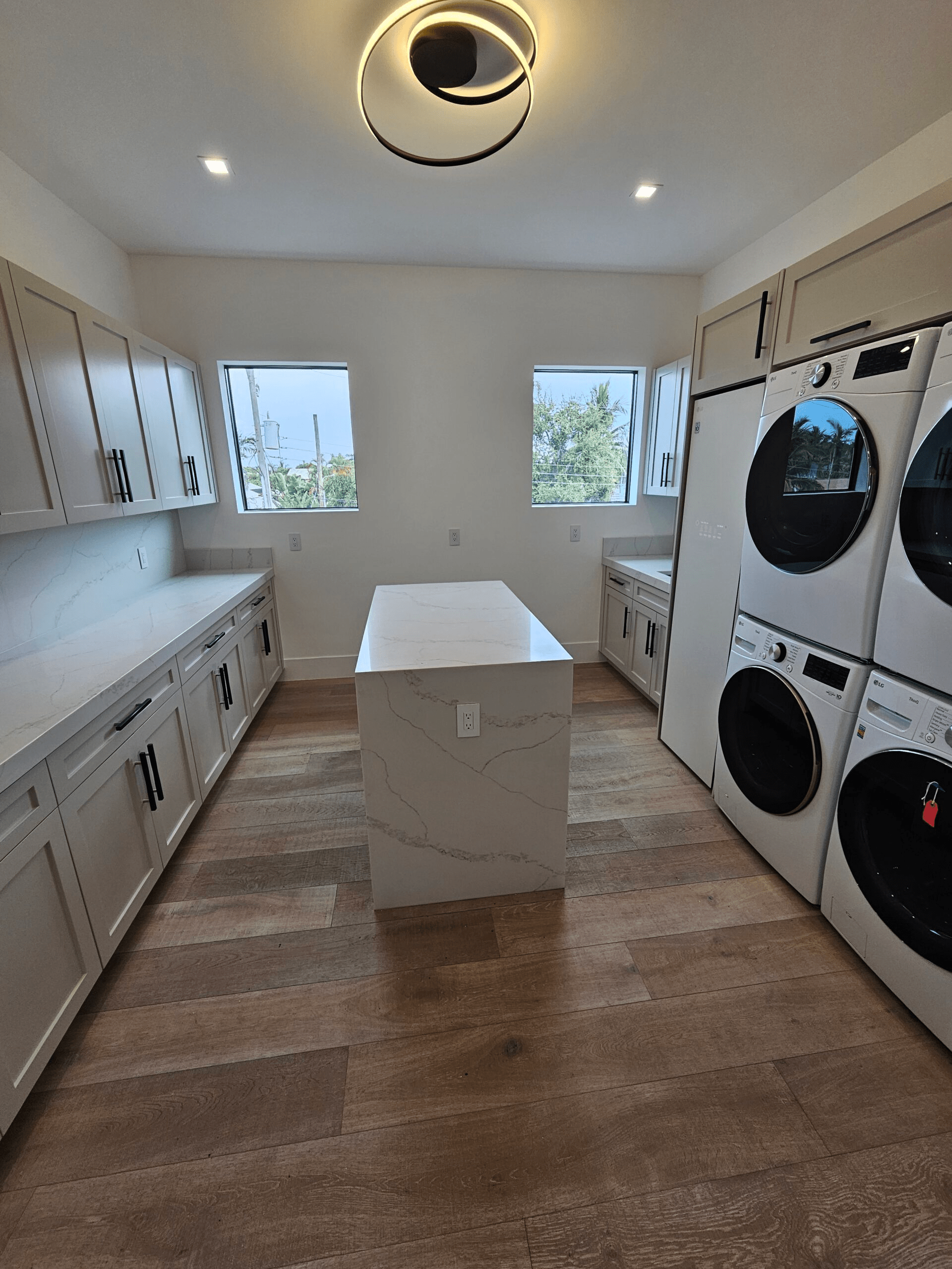 A modern renovated laundry and utility room. Four stacked laundry units sit on one wall across from open counter space.