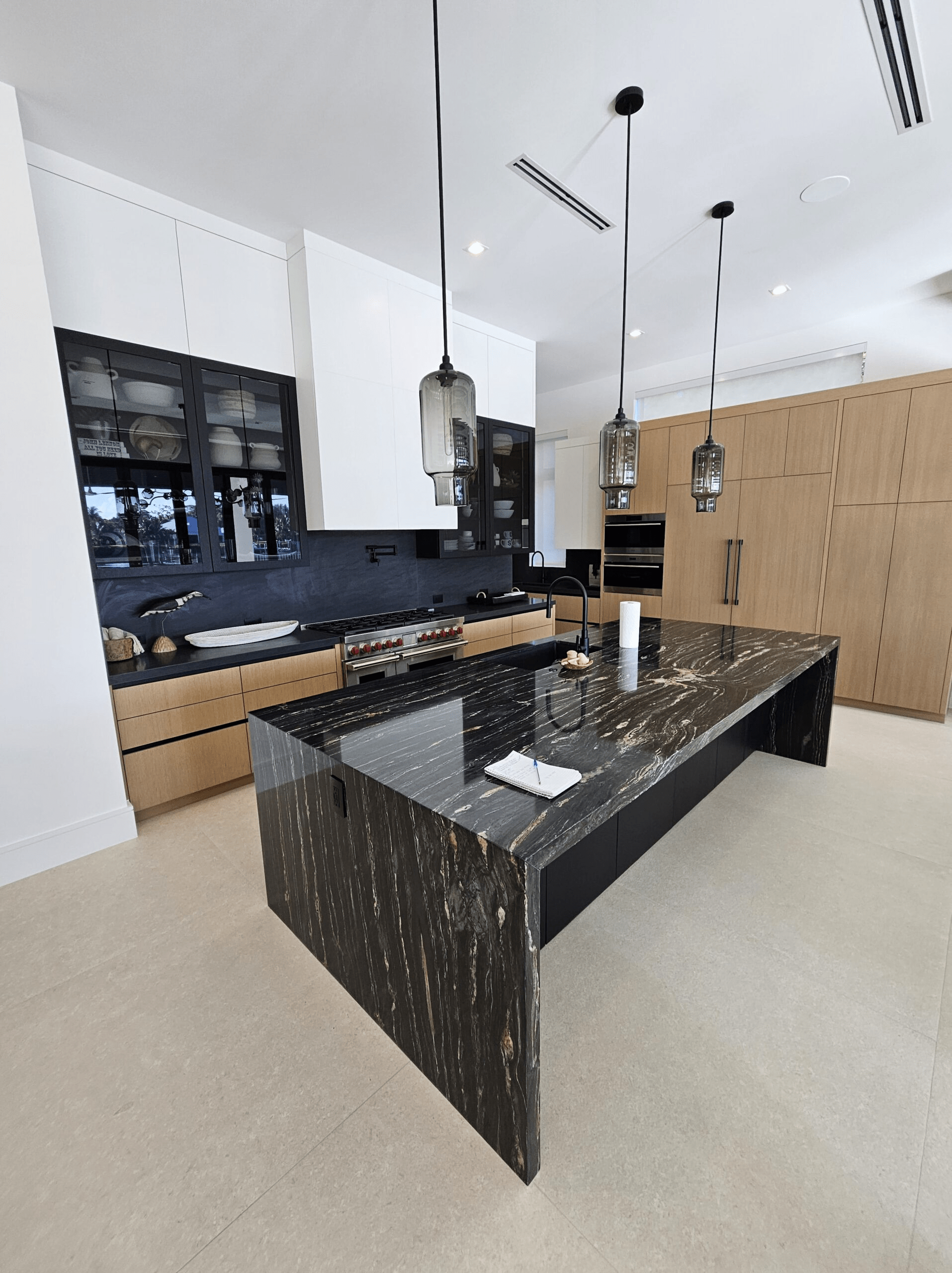 A modern kitchen space with a large stone island and pendant lights.