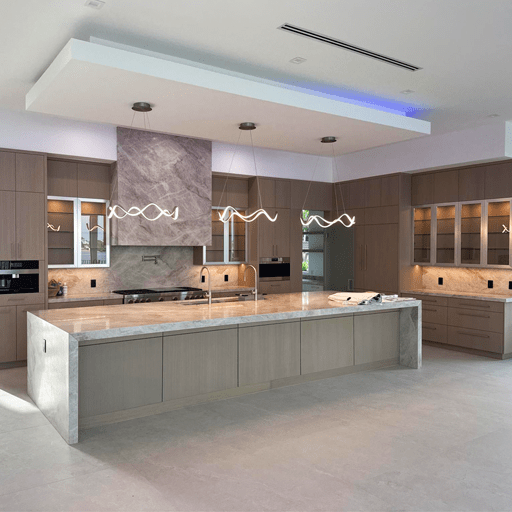 A full kitchen post-remodel. The kitchen is a modern layout with gray stone accents. The center Island is marble and three modern light fixtures hang over the island.