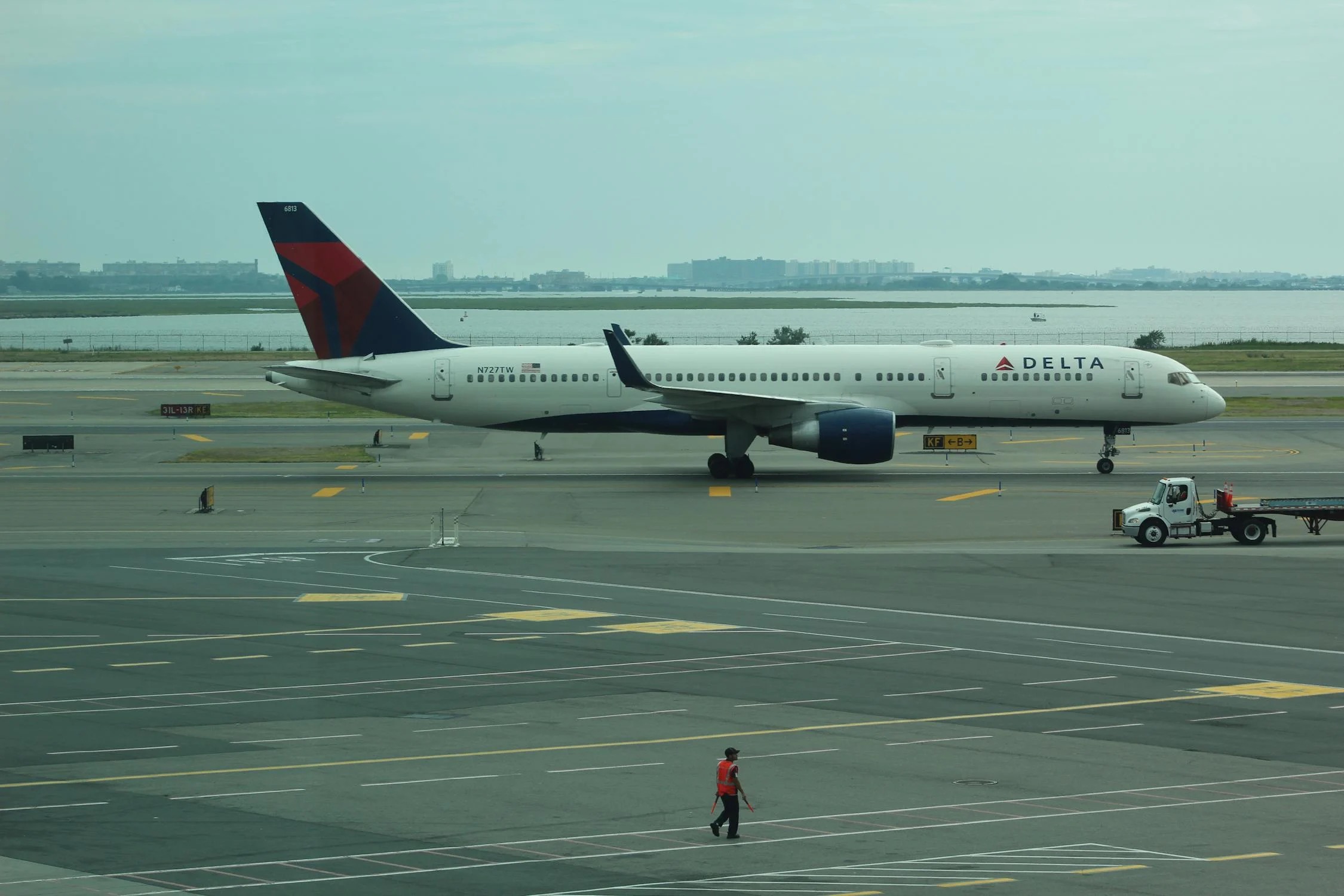 Delta Air Lines Boeing 757-200 taxiing at JFK Airport in New York, with ground crew in foreground.
