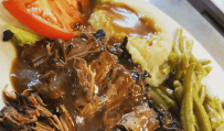 Keysbite meatloaf on a plate with green beans and mashed potatoes and gravy with a tomato slice