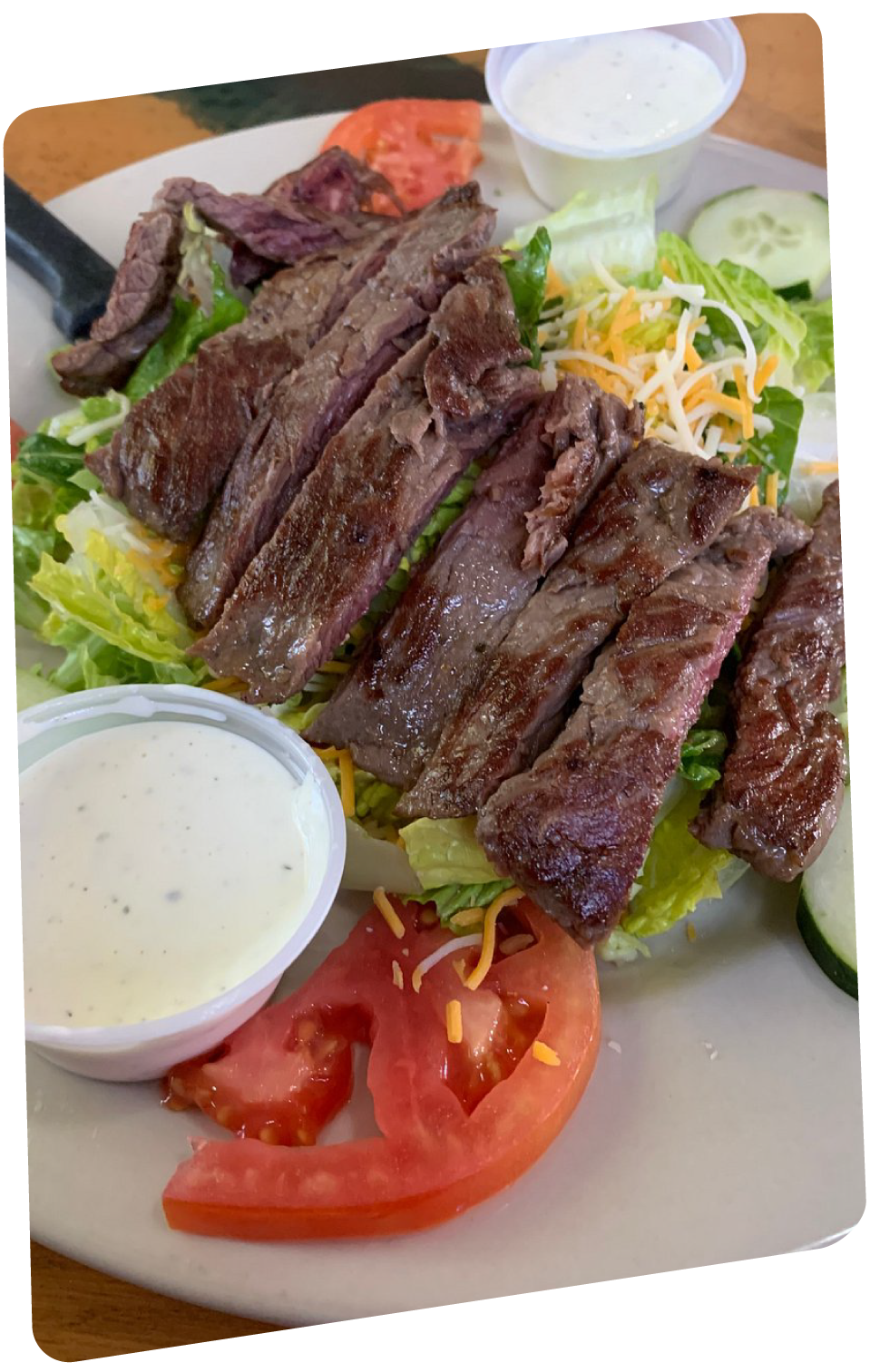 Sliced steak over salad greens with tomatoes, shredded cheese, and dressing