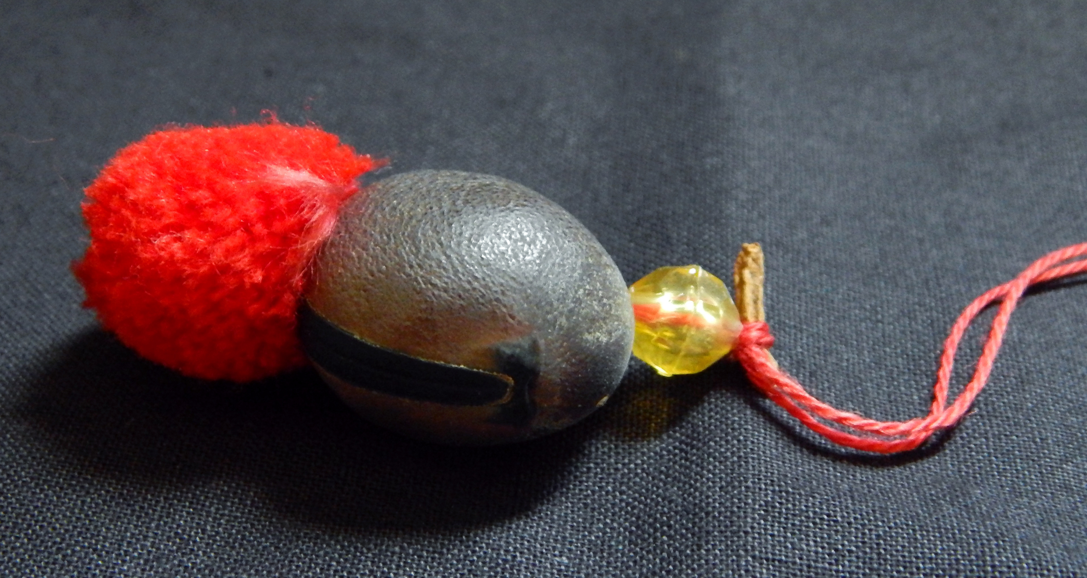 Protection of infant-worn around neck-Mexico/USA-Mexican/Indigenous-Velvet bean or cowhage (Mucuna pruirens), yellow stone, red string and pompom-Seed pod-3/4"