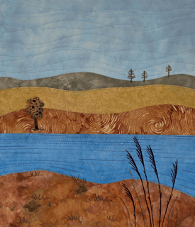 Fabric landscape with blue sky, rolling brown hills, and trees
