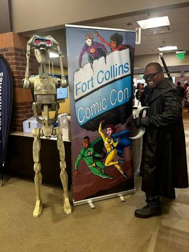 a cosplayer and a robot by a poster.