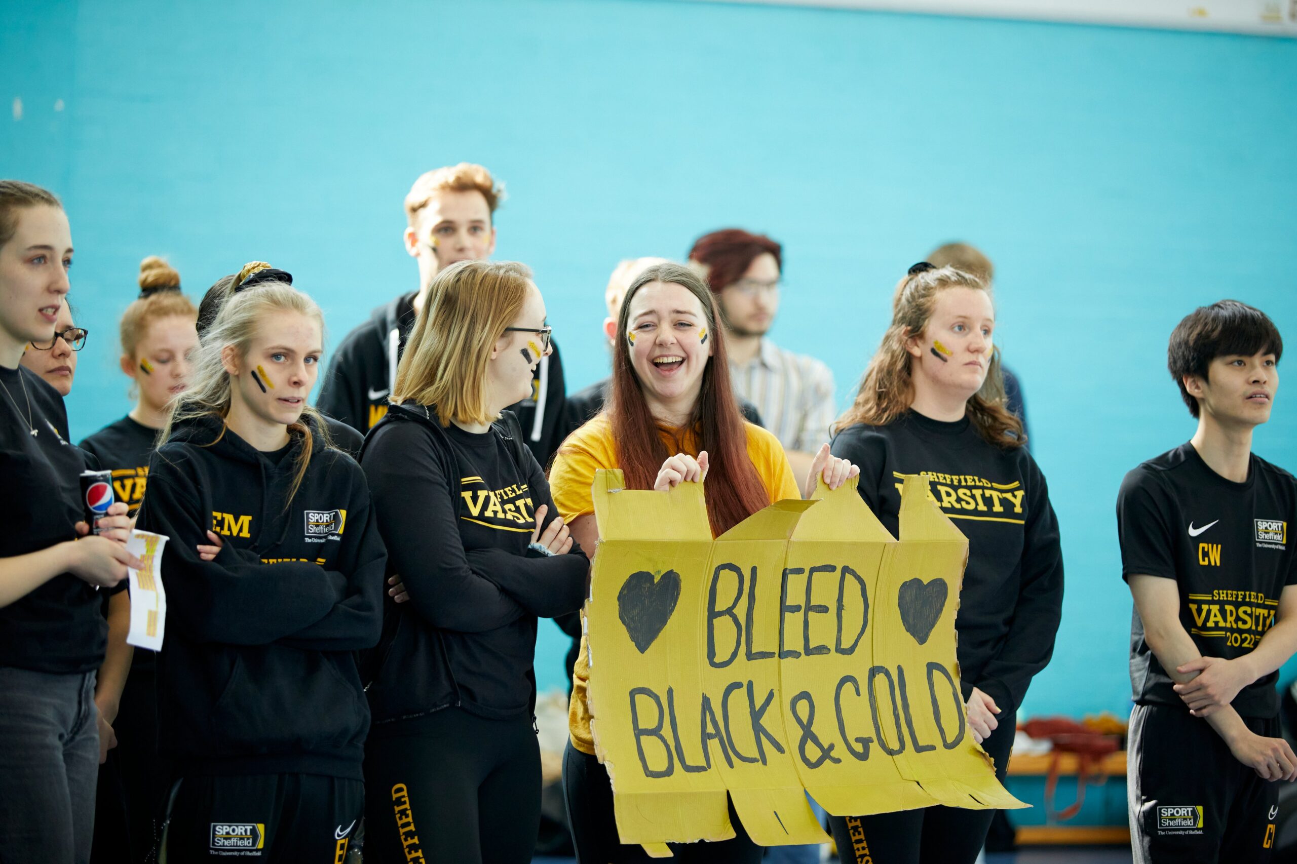 A picture of supports of the University of Sheffield Varsity team, holding up a banner reading "Bleed black and gold"