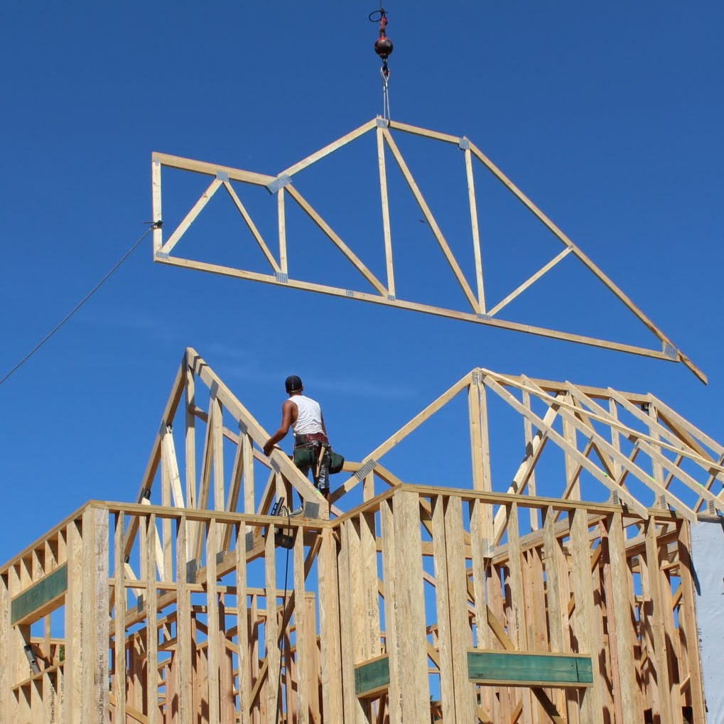 Roof truss hoisted by crane against blue sky during Glen Lake home framing