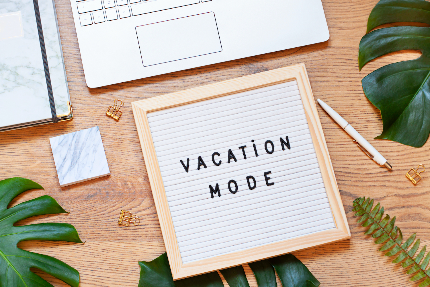 board that reads vacation mode on top of a desk with office supplies