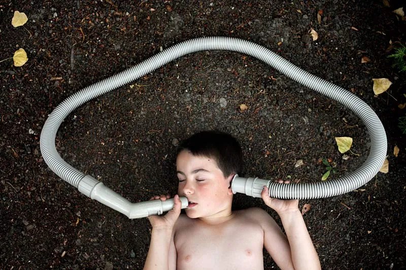 boy with vacuum hose near his mouth and the other end at his ear