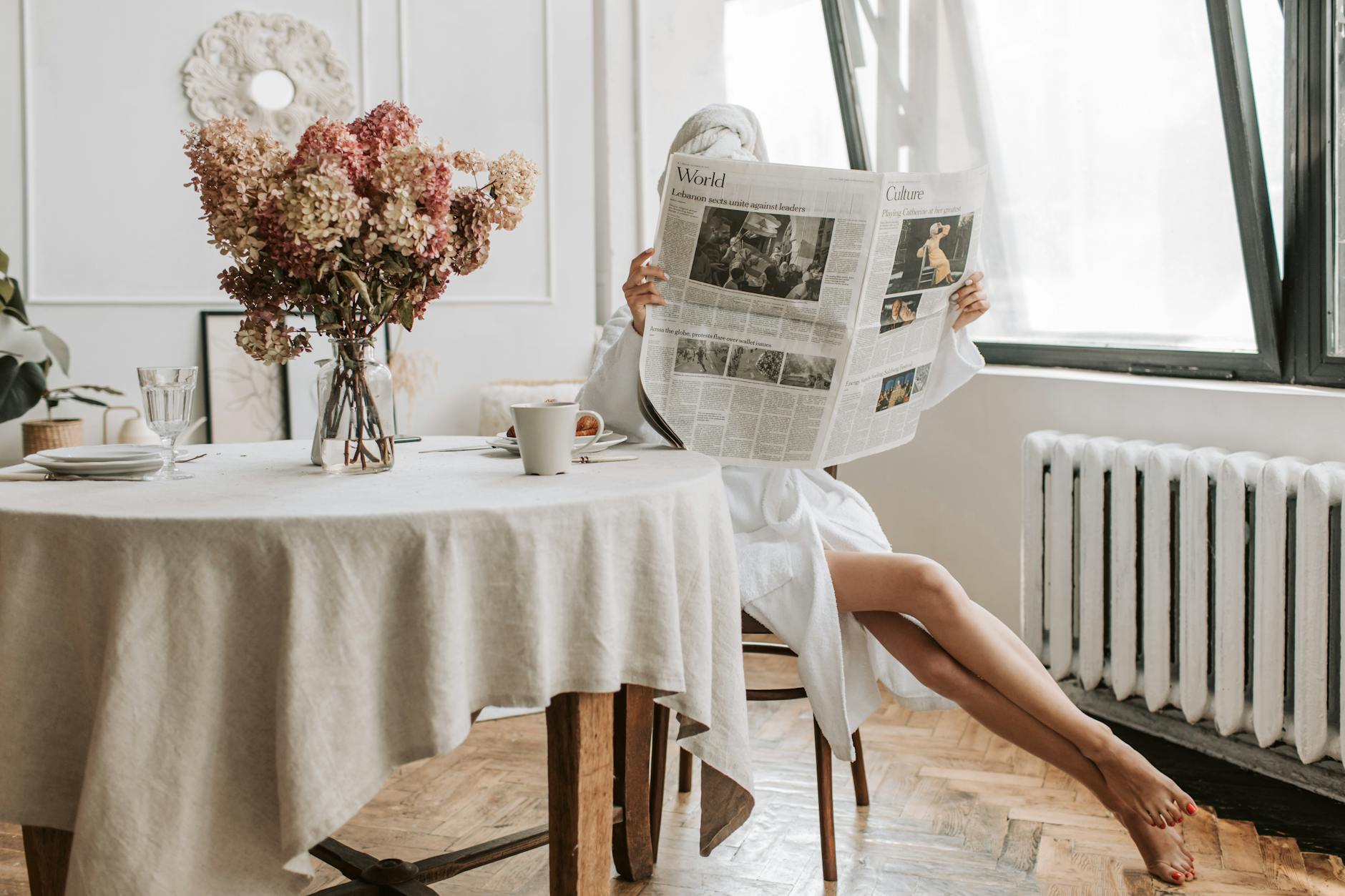 person in white robe sitting on brown chair while holding a newspaper