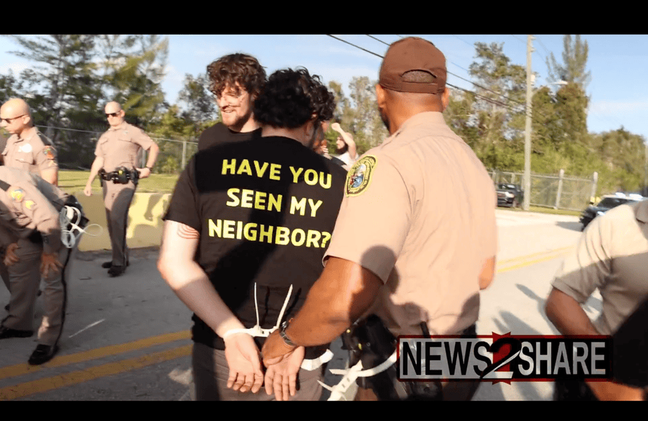 Screenshot of a person being arrested and wearing a black t-shirt with the words, "Have you seen my neighbor?"