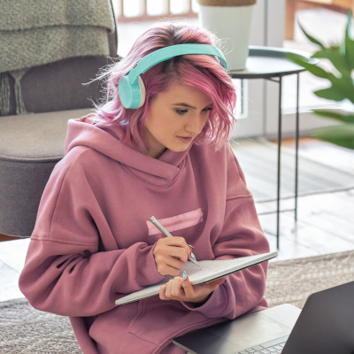 Focused teen girl wear headphones watching webinar online sit on floor at home.