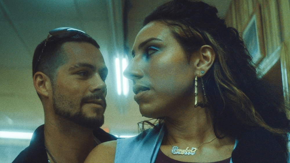 A trans woman stares back at a flirtatious young man behind her played by Dylan O'Brien in the film Ponyboi. 