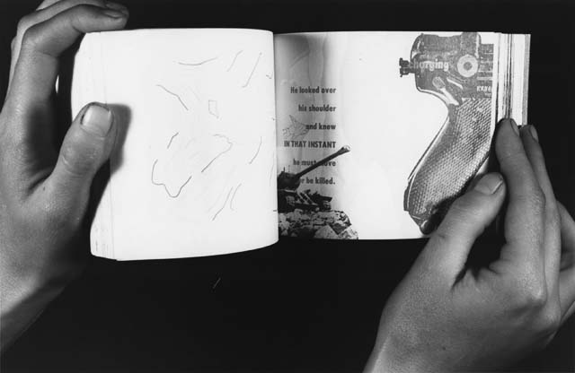 A black and white photograph of someone's hands holding a small, open book. The right page of the book has a partial image of a hand-gun and some text.