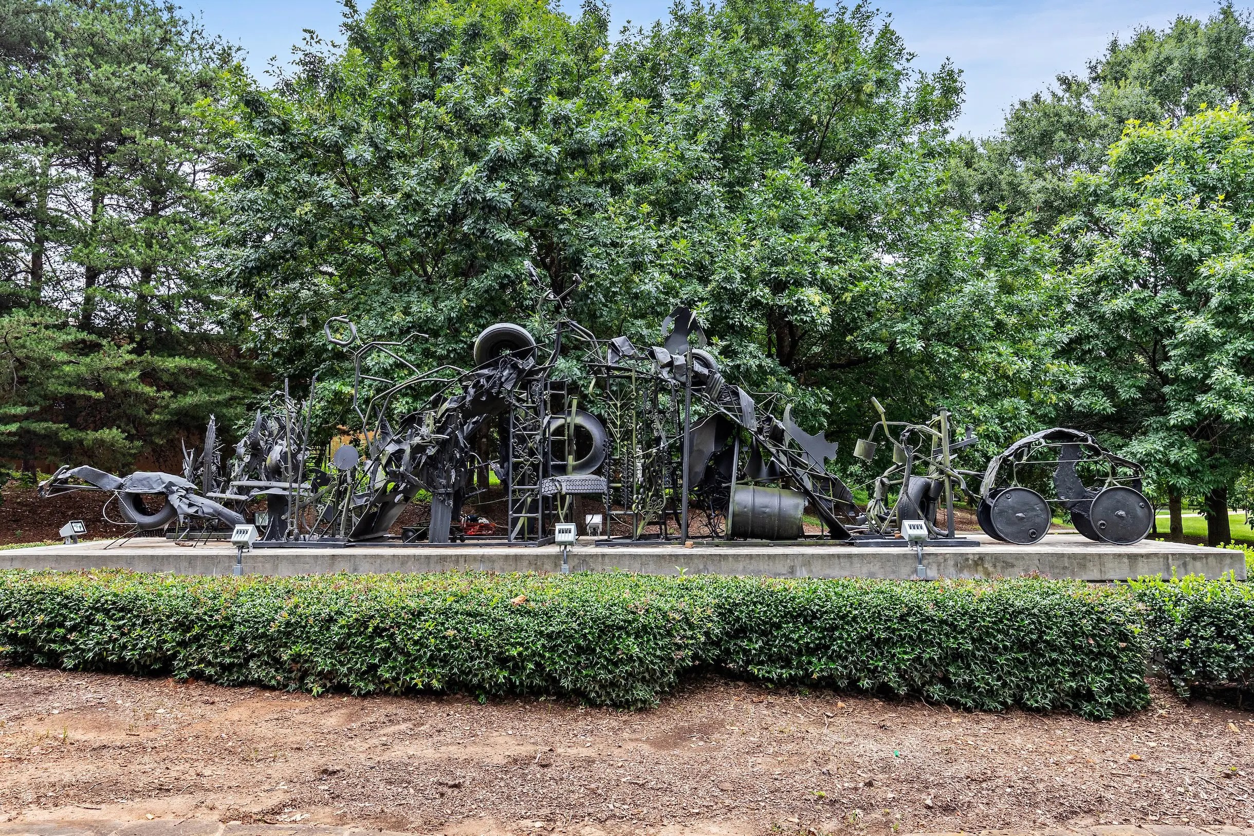 A structure of found objects and steel rises from the ground to form the shape of an arched bridge.