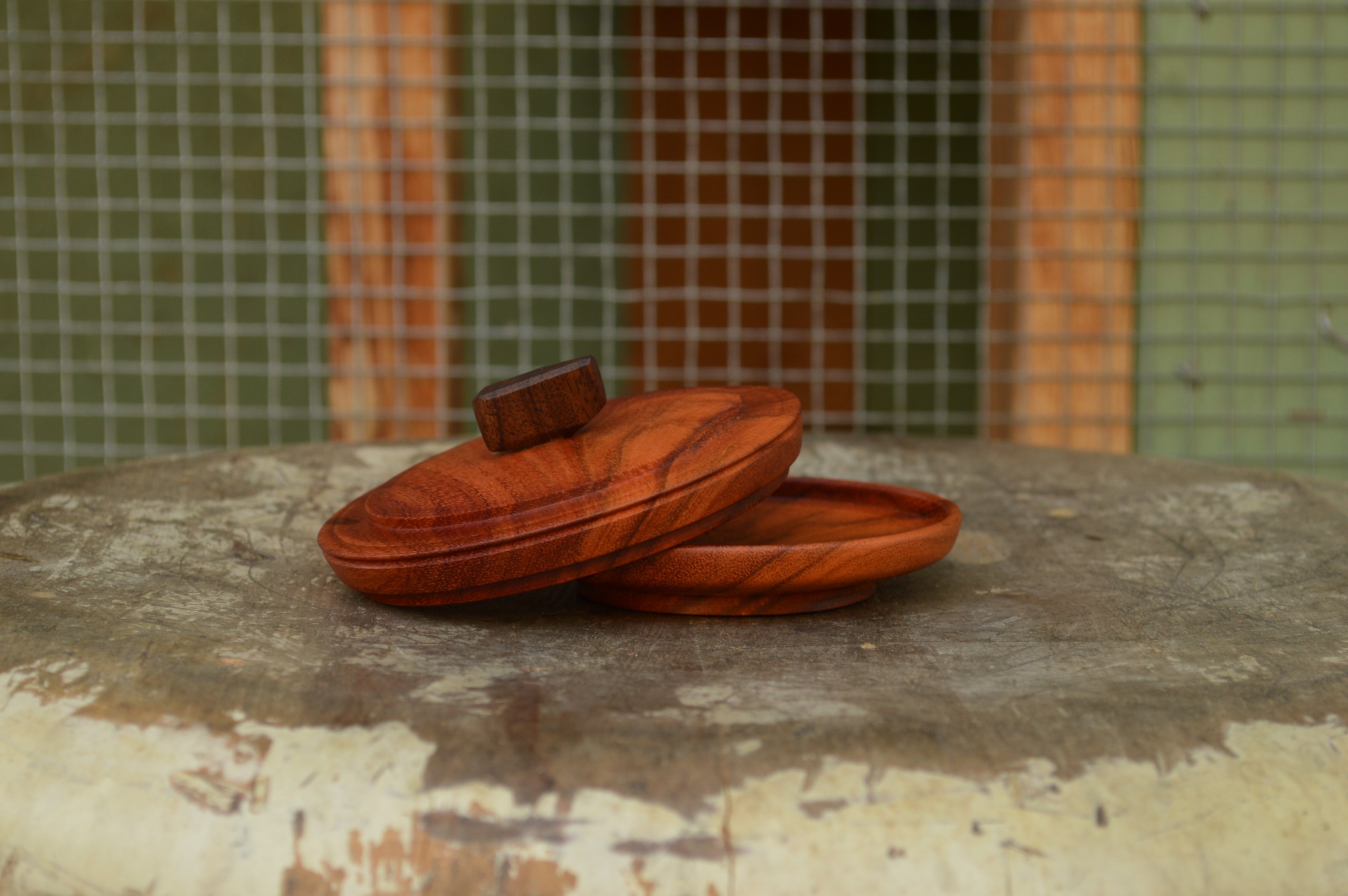 A shallow carob wood container complete with a decorative lid, hand-turned on a lathe and finished with a reclaimed Bay Area walnut handle.