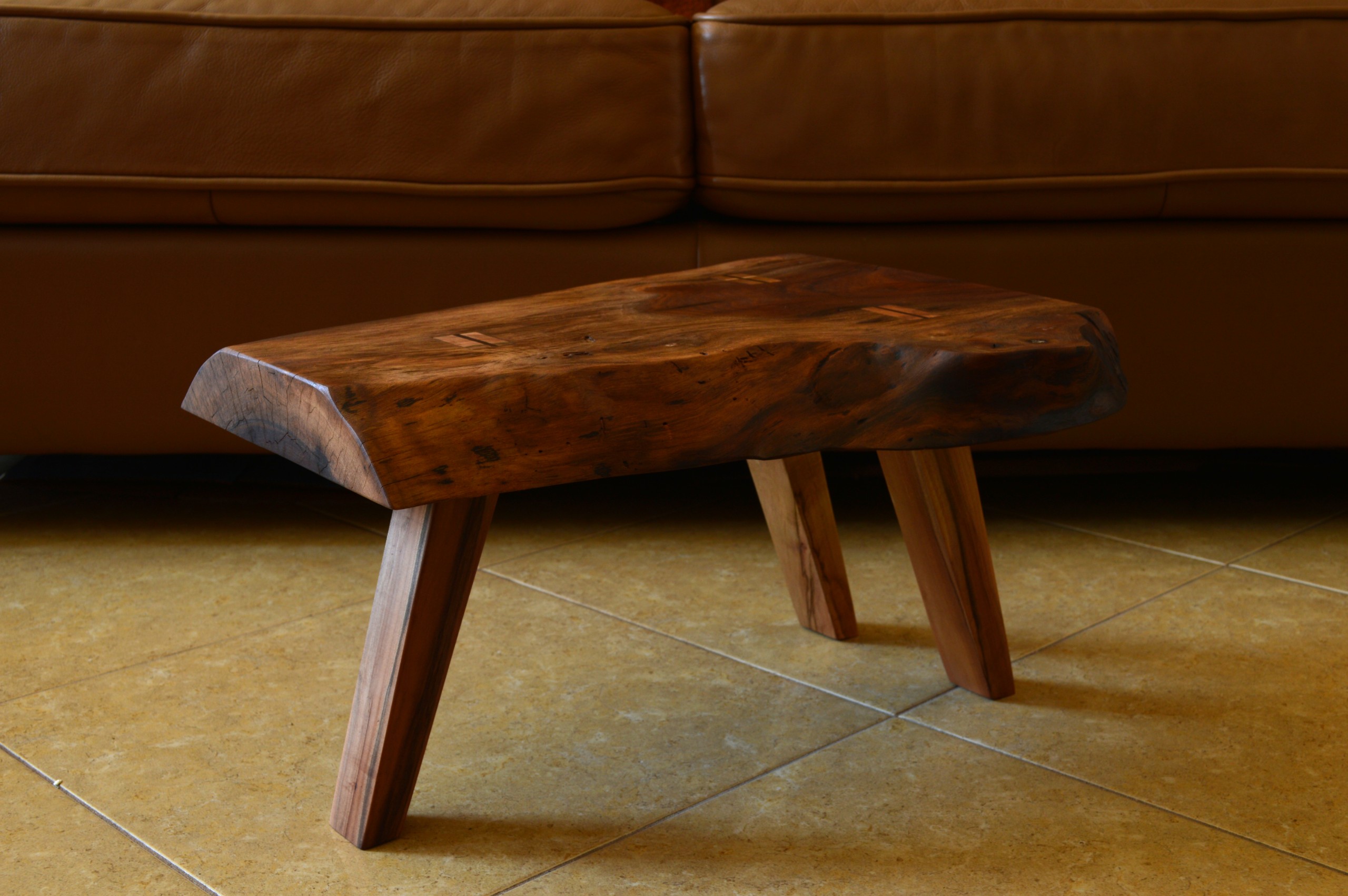 A live-edge walnut slab low side table handcrafted with Japanese-inspired joinery with three maple wood legs in a mid-century style sits in a living room.