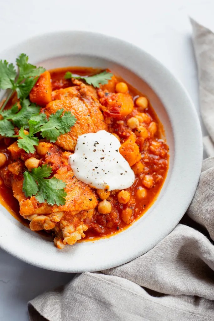 A bowl of harissa chicken stew garnished with fresh cilantro and a dollop of creme fraiche.