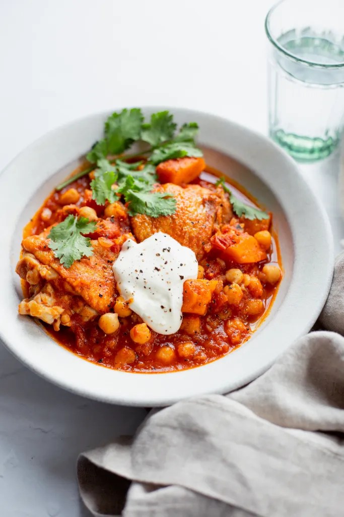 A bowl of harissa chicken stew garnished with fresh cilantro and a dollop of creme fraiche.