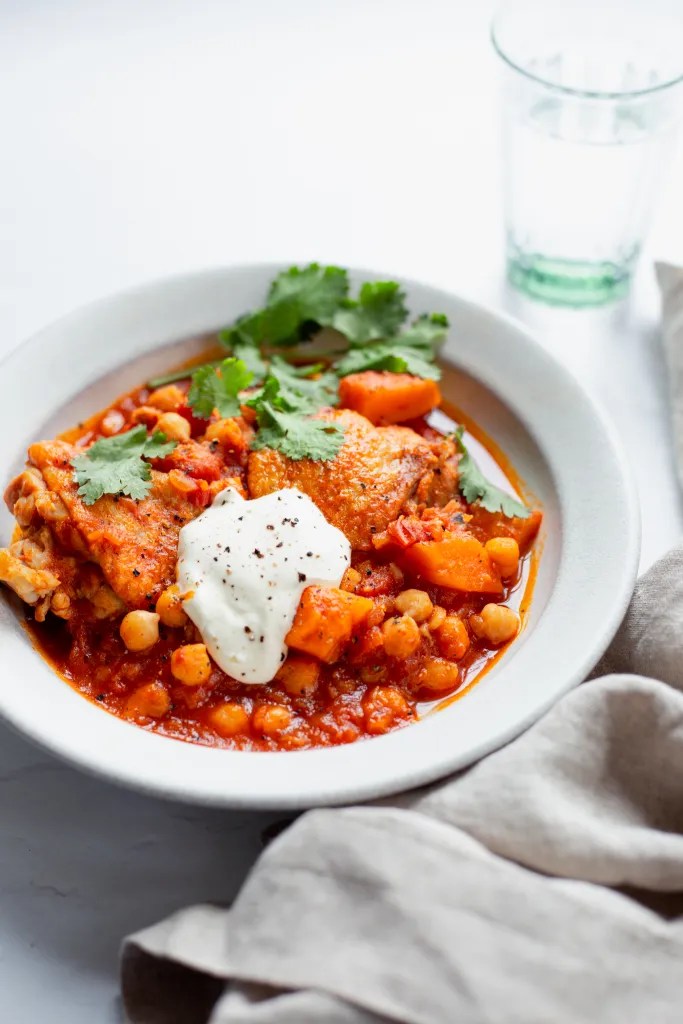 A bowl of harissa chicken stew garnished with fresh cilantro and a dollop of creme fraiche.
