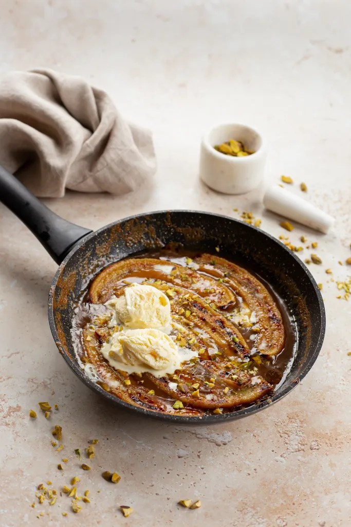 Caramelized miso bananas in a skillet, topped with vanilla ice cream