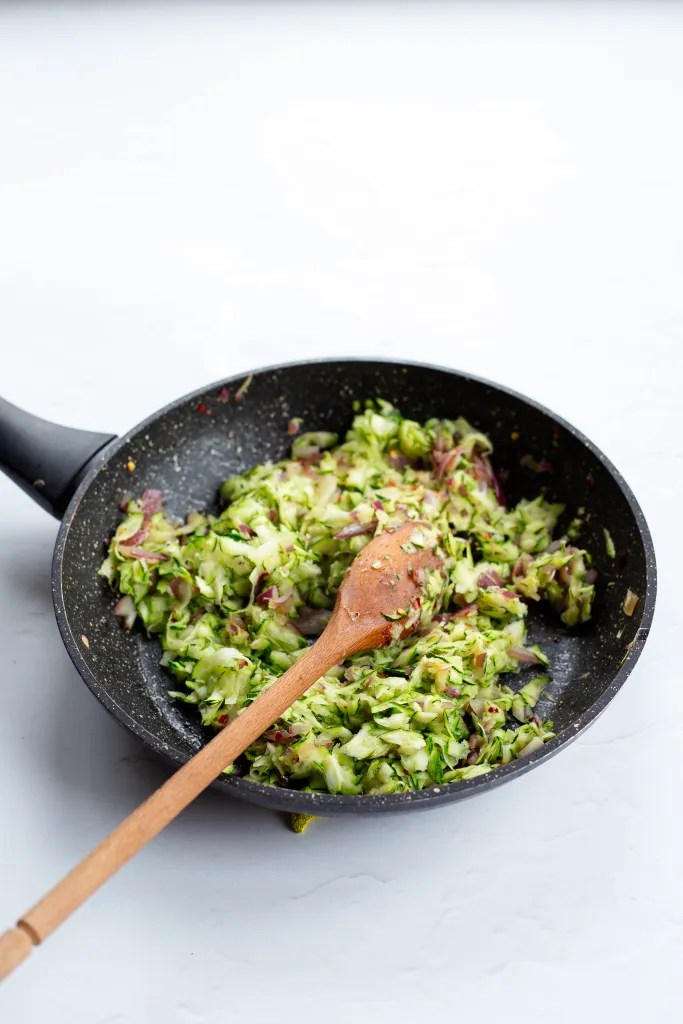 Grated zucchini being sautéed in a skillet.