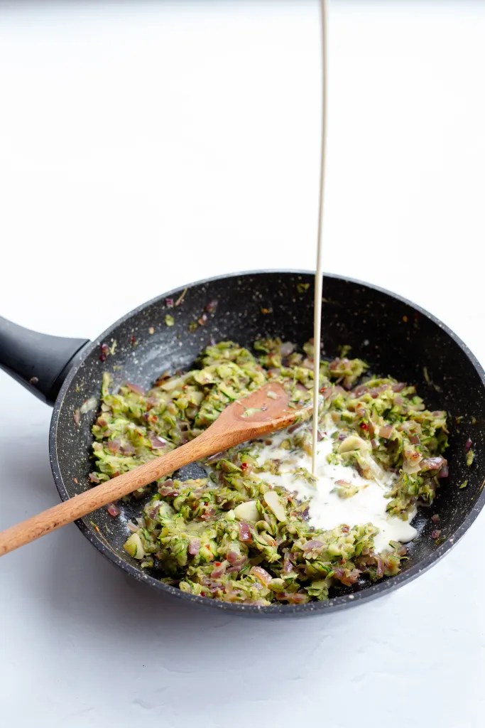 Pouring heavy cream in zucchini pasta sauce.