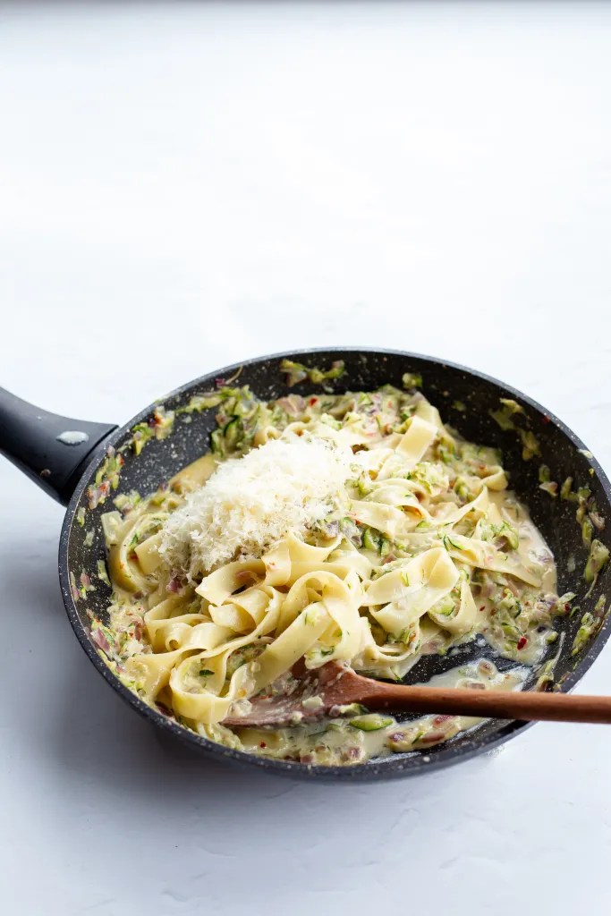 Tossing pasta and parmesan into creamy zucchini sauce.