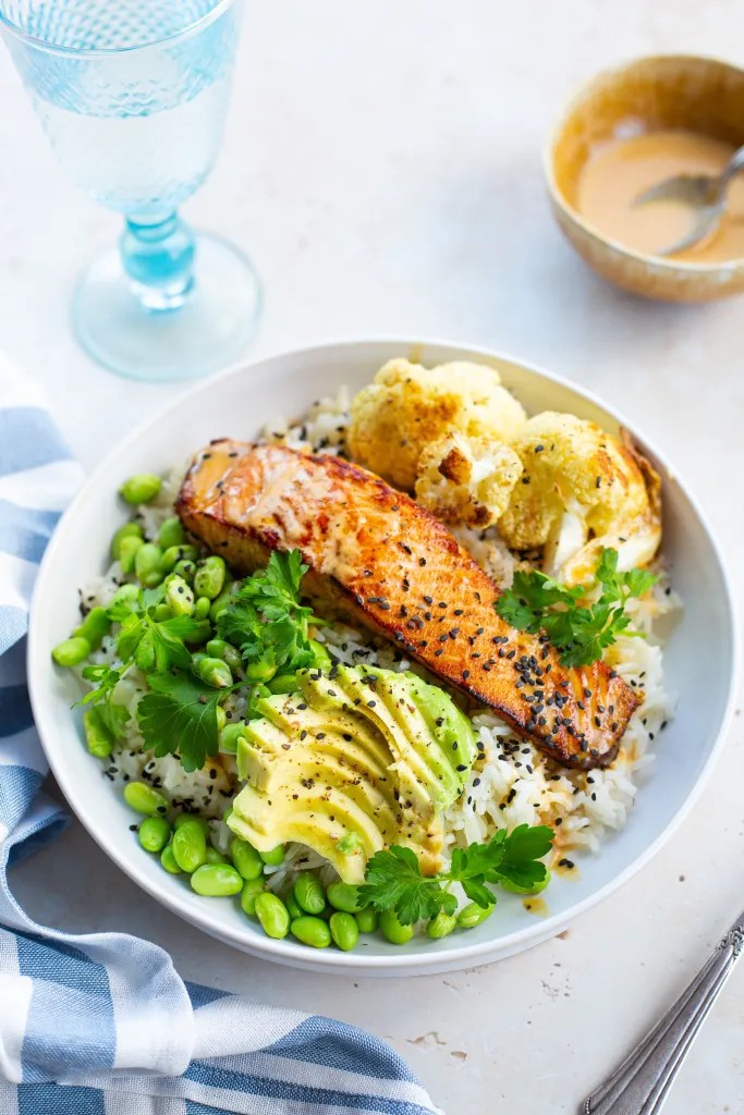 Salmon rice bowl topped with cauliflower, avocado, edamame, and miso mayo drizzle