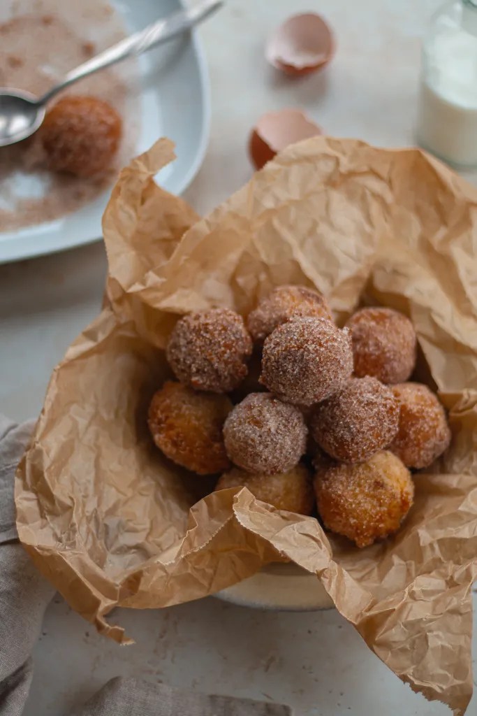 Shot of golden-brown buttermilk drop donuts heavily coated in cinnamon sugar, stacked on a serving plate.