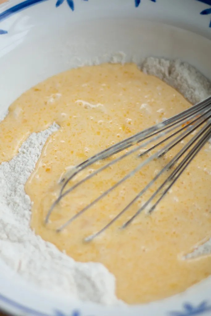 A whisk folding the wet buttermilk mixture into the dry flour ingredients.