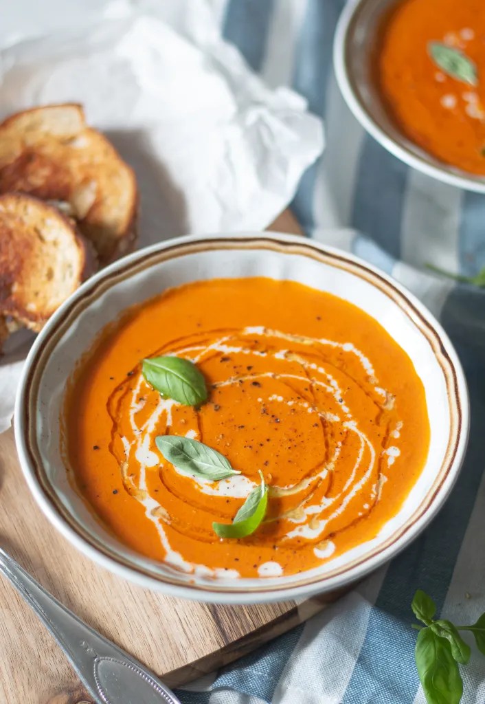 a bowl of roasted tomato soup garnished with heavy cream and fresh basil