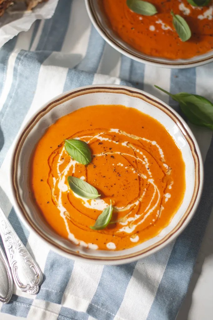 a bowl of roasted tomato soup garnished with heavy cream and fresh basil
