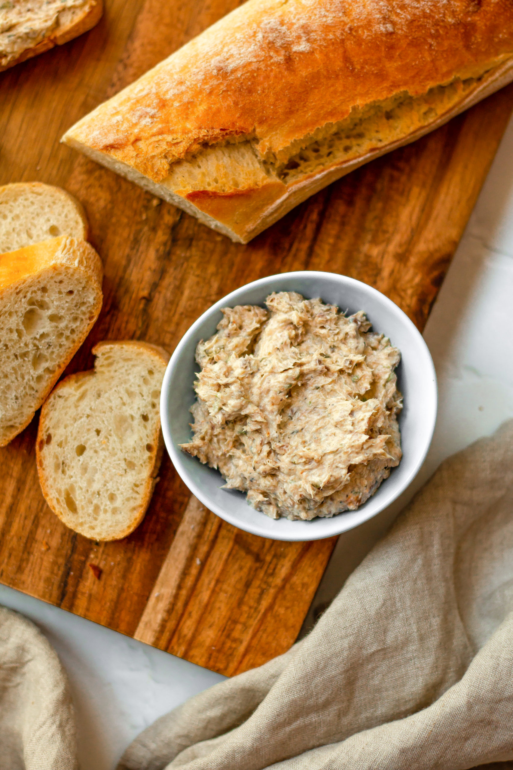 overhead shot of sardine spread served in a small bowl next to sliced of baguette