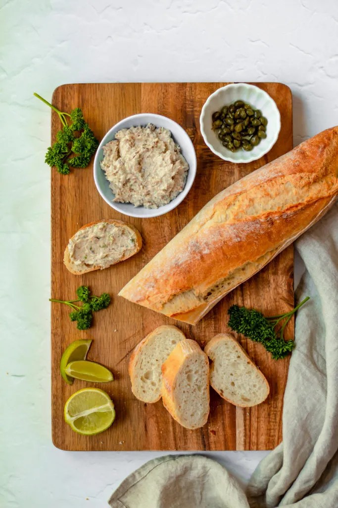 Sardine spread in a bowl and baguette served on a cutting board.