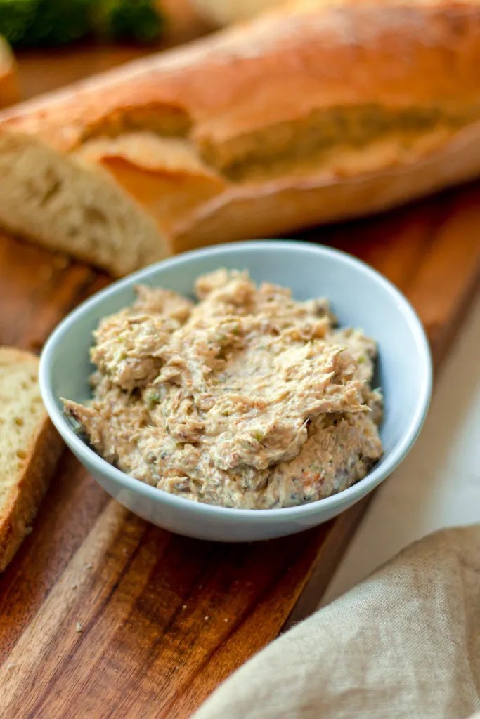 sardine spread served in a small bowl next to a baguette on a cutting board
